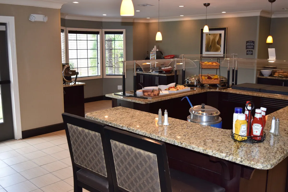 A spacious breakfast area with a breakfast bar and buffet display, complemented by cozy window seating. Guests are seen socializing and enjoying their meals, creating a lively yet comforting scene that reflects the flexibility of shared and solo dining.