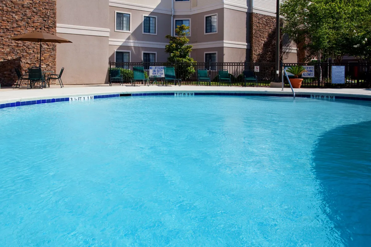 A lively exterior scene highlighting the swimming pool, outdoor seating area, and the building's facade. The sunny environment suggests spaces for relaxation and informal networking outside of meetings.