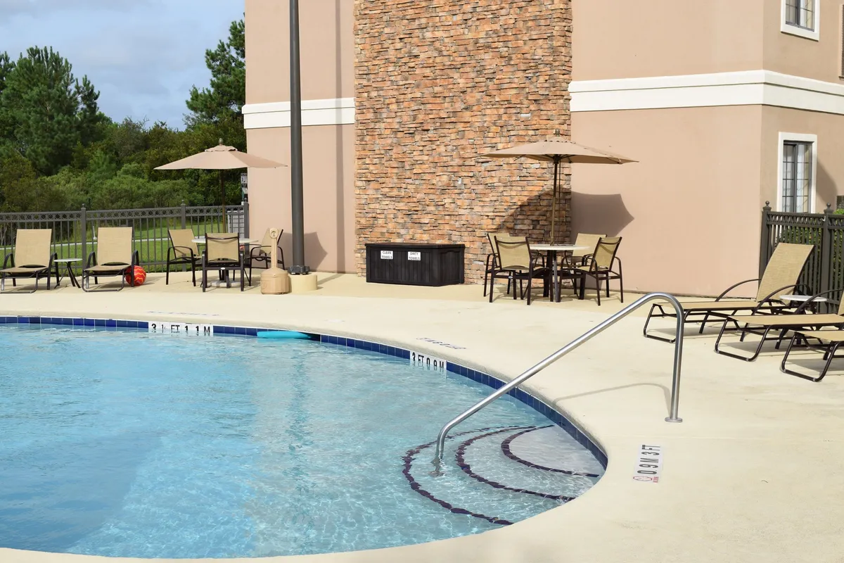 This exterior image features a sparkling swimming pool surrounded by a stone wall, with inviting lounge chairs and umbrellas offering ample space for sunbathing or relaxing. The ambiance suggests both daytime fun and evening gatherings under the stars.