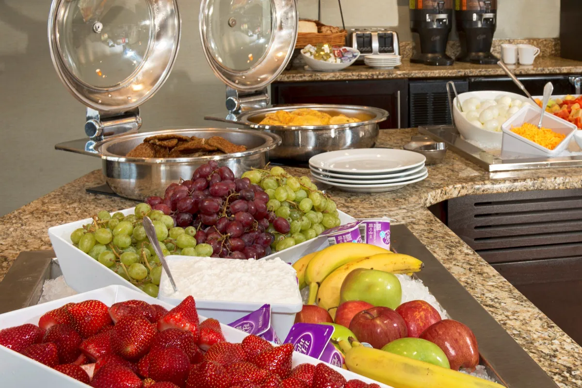 A cheerful breakfast scene with a variety of fresh fruits, ready-to-eat breakfast items, and a coffee station. The setup is designed for easy access and encourages gathering, reflecting a friendly and energetic start to the day.