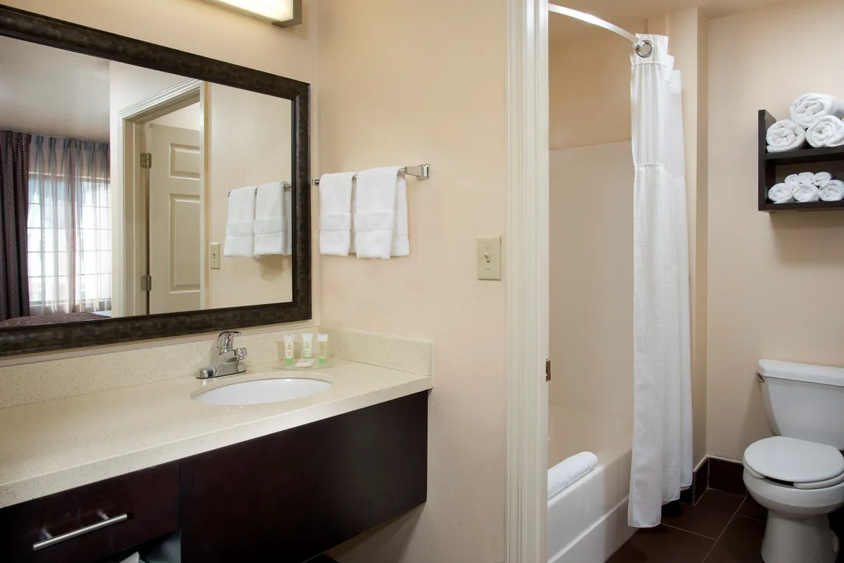 This image features a serene vanity and shower area, complete with a tidy towel rack and a well-lit mirror. The inviting, peaceful atmosphere suggests a space ideal for unwinding and refreshing after an eventful day.