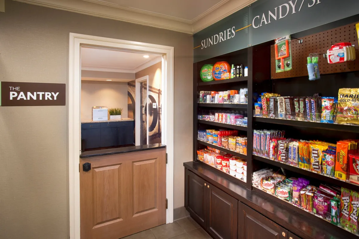 This image captures 'THE PANTRY'—an on-site convenience area filled with snacks and sundries, visible through open shelving and signage. The scene suggests easy access to essentials for guests, and the open door hints at connectivity to additional amenities or communal spaces.