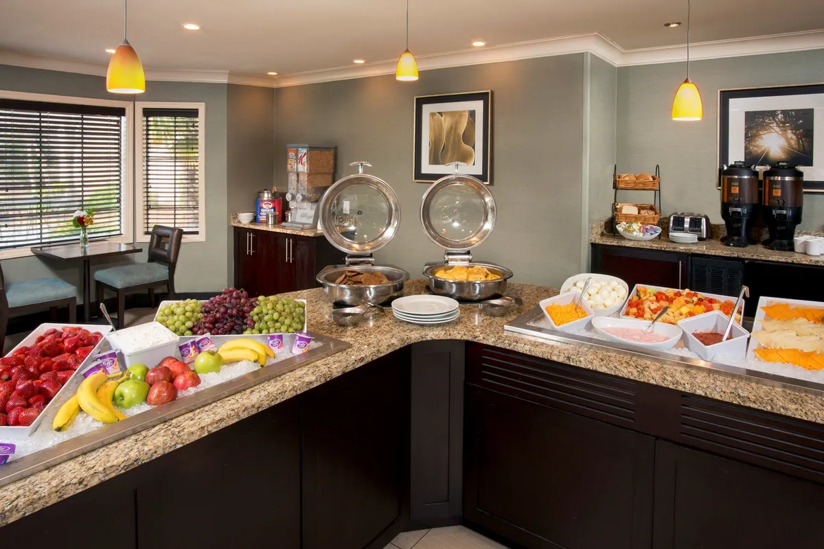 A close-up view of a vibrant breakfast buffet featuring a colorful fruit display, a range of hot breakfast items, and a well-stocked coffee station. The set-up conveys a welcoming atmosphere ideal for guests to start their day, with inviting lighting and a sense of abundance.