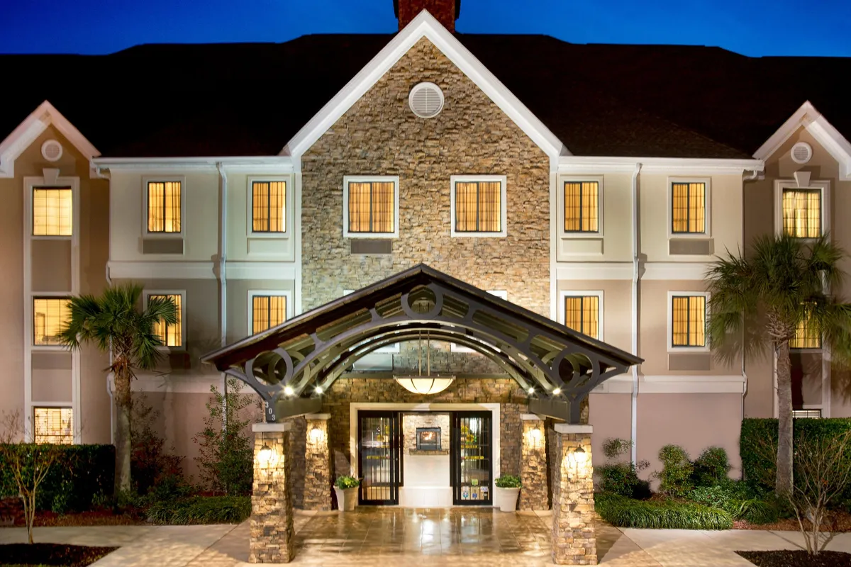 The photograph showcases a beautifully lit hotel exterior with a stone façade, arched entrance, and glowing windows, evoking a sense of security and welcome for guests arriving in the evening.